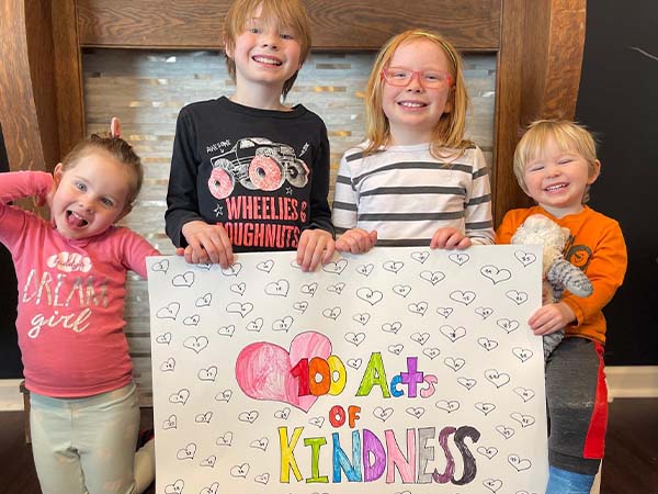 Four children holding a 100 Acts of Kindness poster