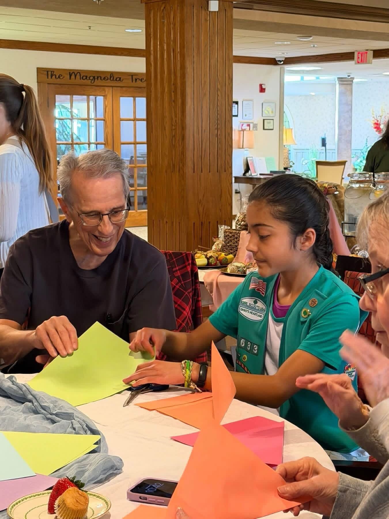 A Girl Scout and older adults making spring paper crafts together at a tea party at Chapel Grove Inn